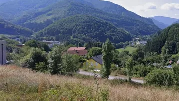 Malerische Berglandschaft mit bewaldeten Hügeln, vereinzelten Häusern und weitem Blick in die Natur.