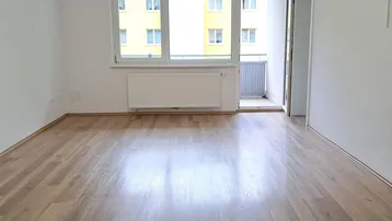 Helles, leeres Wohnzimmer mit Laminatboden und Zugang zu einem kleinen Balkon.