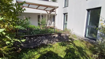 Gepflegter Gartenbereich mit Hochbeeten und einer einfachen Holzpergola neben dem modernen Gebäude.