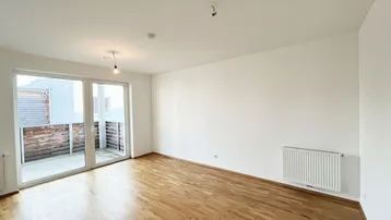 Heller Wohnraum mit Parkettboden, weißen Wänden und Zugang zu einem Balkon.