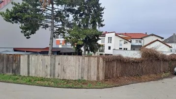Blick auf die Grundstücksgrenze mit Holzzaun und umliegenden Gebäuden in ländlicher Umgebung.