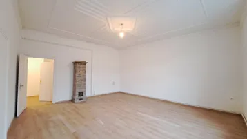 Geräumiges, leeres Wohnzimmer mit hellem Laminatboden und dekorativer Deckenverzierung.