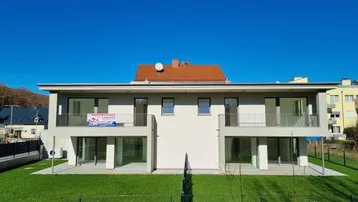 Modernes Doppelhaus mit großzügigen Fensterfronten und Gartenfläche, umgeben von Natur.