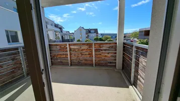 Geräumiger Balkon mit Holzsichtschutz und Blick auf die umliegenden Gebäude unter blauem Himmel.