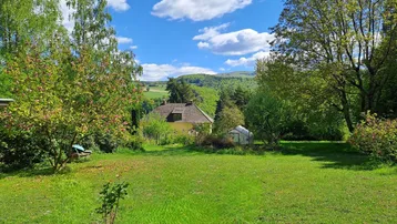 Weitläufiger Gartenbereich mit viel Grün und Blick auf das Haus und die umliegende Landschaft.