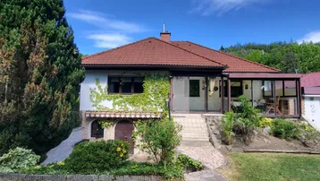 Charmantes Einfamilienhaus mit begrüntem Wintergarten und gepflegtem Vorgarten unter blauem Himmel.