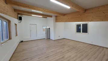 Geräumiger, heller Innenraum mit hohen Decken, sichtbaren Holzbalken und modernem Laminatboden.