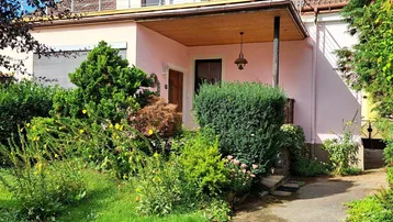 Traditionelles Haus mit gepflegtem Vorgarten und Dachterrasse unter blauem Himmel.