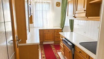 Traditionelle Holzküche mit hellen Arbeitsplatten, Einbaugeräten und rotem Läufer.