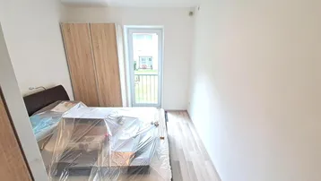 Schlafzimmer mit Holzboden, Kleiderschrank und Zugang zu einem französischen Balkon.