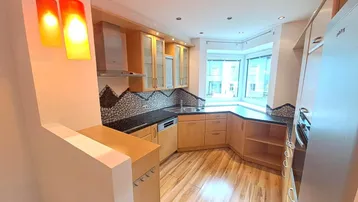 Helle Küche mit Holzschränken, dunklen Arbeitsplatten, Mosaikfliesen und einem Erkerfenster.