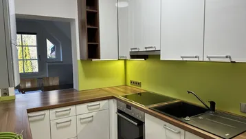 Moderne Küche mit weißen Hochglanzfronten, Holztheke und grüner Spritzschutzwand unter Dachschrägen.