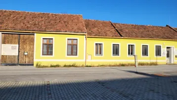 Gelbes Gebäude mit braunem Ziegeldach und Holztor unter blauem Himmel.