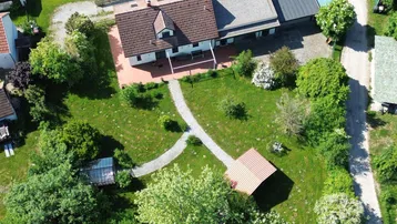 Luftaufnahme eines Hauses mit weitläufigem Garten, gepflasterten Wegen, einem Gewächshaus und einem Gartenhaus.