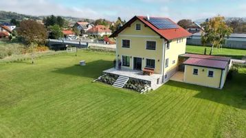 Luftaufnahme des gelben Hauses mit rotem Dach, Photovoltaikanlage und weitläufigem Garten.