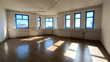 Heller Büroraum mit Holzboden und mehreren Fenstern, die viel Tageslicht hereinlassen.