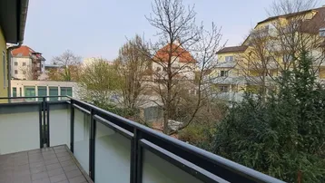 Geräumiger Balkon mit Fliesenboden und Blick ins Grüne sowie auf umliegende Gebäude.