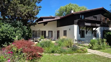 Großzügiges Einfamilienhaus mit gepflegtem Garten und üppiger Bepflanzung unter blauem Himmel.