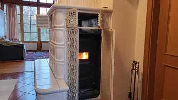 Wohnzimmer mit traditionellem Kachelofen, Holzboden und großen Fenstern.