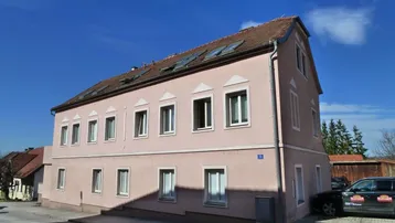 Gut erhaltenes Wohngebäude mit rosa Fassade, Satteldach und Dachfenstern in ländlicher Umgebung.