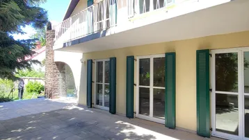 Große gepflasterte Terrasse vor dem Haus mit grünen Fensterläden und Balkon im Obergeschoss.