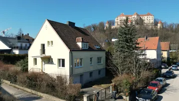 Freistehendes Haus mit Satteldach und Blick auf die historische Burg im Hintergrund.