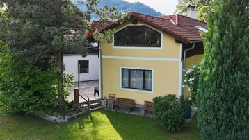 Gelbes Haus mit rotem Ziegeldach und gepflegtem Vorgarten, umgeben von Bäumen.