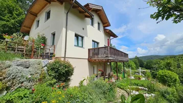 Charmantes Haus mit Balkon und gepflegtem Garten, umgeben von üppiger Natur und grüner Landschaft.
