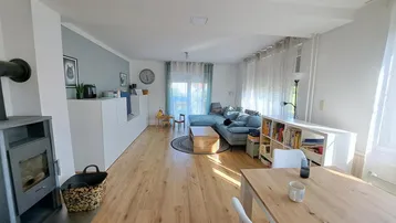 Heller offener Wohn-Essbereich mit Holzboden, Kaminofen und modernem Sofa.