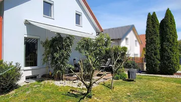 Ansicht des Hauses von außen mit einer Terrasse und einem gepflegten Gartenbereich unter blauem Himmel.