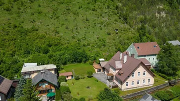Luftaufnahme eines Anwesens mit mehreren Häusern, umgeben von grünen Hügeln und Bäumen.