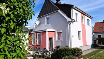 Außenansicht eines Einfamilienhauses mit Garten, Rasenfläche und farbiger Fassade unter blauem Himmel.