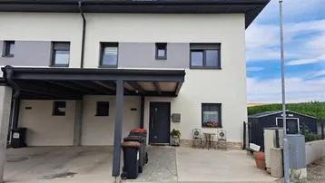 Moderne Reihenhausfassade mit Carport, kleinem Vorgarten und Mülltonnenbereich.