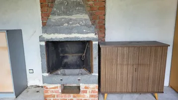 Außenkamin oder Grillplatz aus Stein und Ziegeln mit einem Holzschrank daneben.