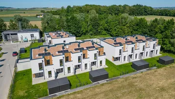 Luftaufnahme moderner Reihenhäuser mit Photovoltaikanlagen auf den Dächern in ländlicher Umgebung.