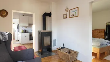 Gemütliches Wohnzimmer mit Holzofen, Holzboden und Blick in die Küche und ein Schlafzimmer.