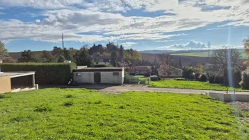 Weitläufiger Gartenbereich mit Rasenfläche und Blick auf die umliegende Landschaft und ein kleines Gebäude.