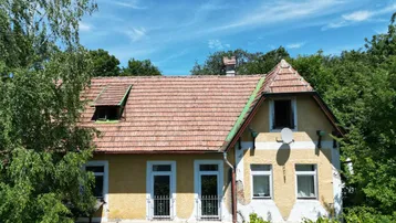 Altes, charmantes Haus mit gelber Fassade, rotem Ziegeldach und umgeben von üppigem Grün.