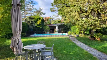 Großer Garten mit Rasenfläche, Sitzbereich und einem umzäunten Swimmingpool im Hintergrund.