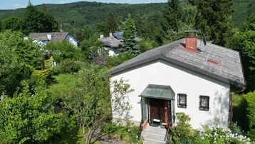 Luftaufnahme eines Einfamilienhauses mit Satteldach, umgeben von üppiger grüner Landschaft und Bäumen.