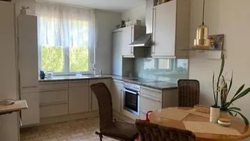 Funktionale Küche mit hellen Einbauschränken, Essbereich und großem Fenster mit Blick ins Grüne.