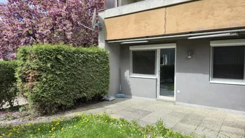 Gepflasterte Terrasse im Erdgeschoss mit Hecke und blühendem Baum, ideal für entspannte Stunden im Freien.