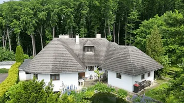 Luftaufnahme eines Hauses mit Teich und üppiger Vegetation, umgeben von hohen Bäumen.