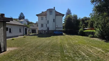 Großes Grundstück mit Einfamilienhaus und Nebengebäude unter blauem Himmel und viel Grün.