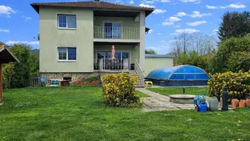 Haus mit großem Garten, Terrasse und überdachtem Pool unter blauem Himmel.