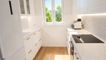 Helle, moderne Küche mit weißen Schränken, Marmorarbeitsplatten und Blick ins Grüne.