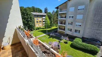 Blick vom Balkon auf die grüne Gemeinschaftsfläche zwischen den Wohngebäuden an einem sonnigen Tag.