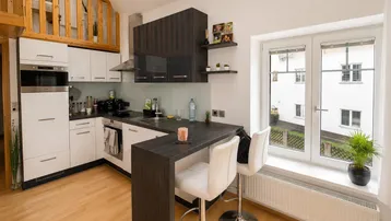 Moderne Küche mit dunklen und weißen Schränken, Frühstücksbar und Blick ins Grüne durch das Fenster.