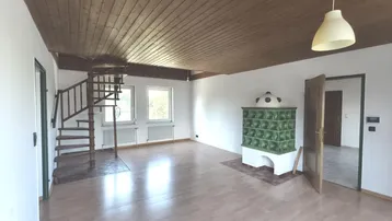 Helles Wohnzimmer mit Holzdecke, Wendeltreppe und traditionellem Kachelofen.