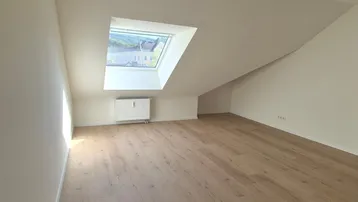 Helles Zimmer im Dachgeschoss mit Holzboden, Dachfenster und schrägen Wänden.